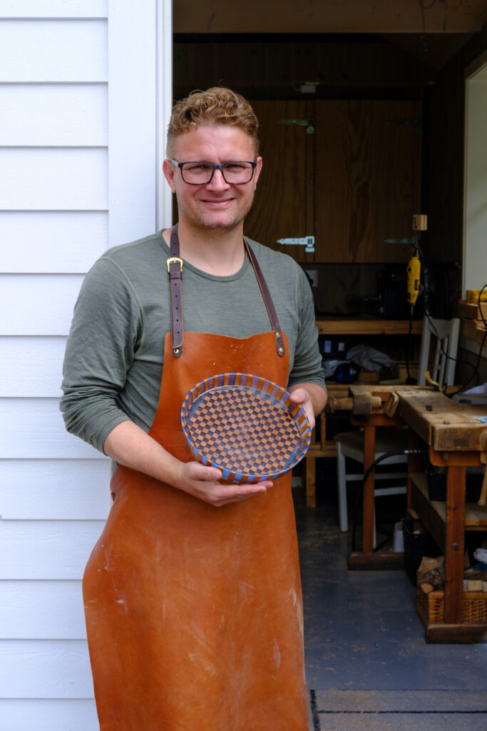 A person wearing an apron holding a bowl made from wood and epoxy resin.

