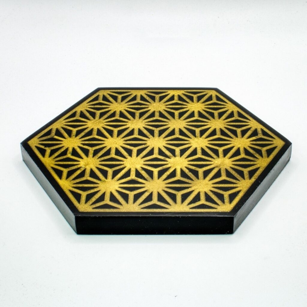 A coaster CNC machined in black acrylic with a Japanese Asanoha pattern and then filled with CCR pigmented with gold mica powder and made with entropy resins epoxy.