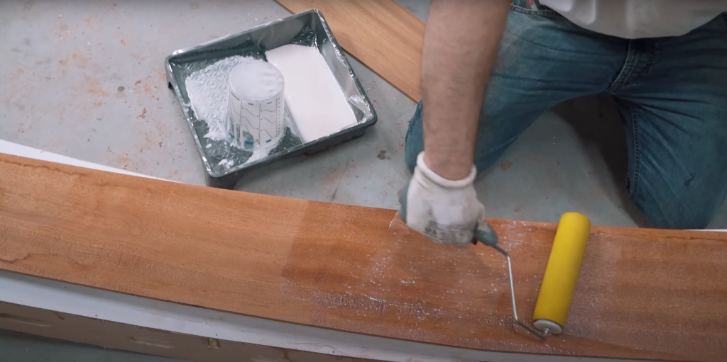 Rolling west system epoxy onto a wooden board for his boat build