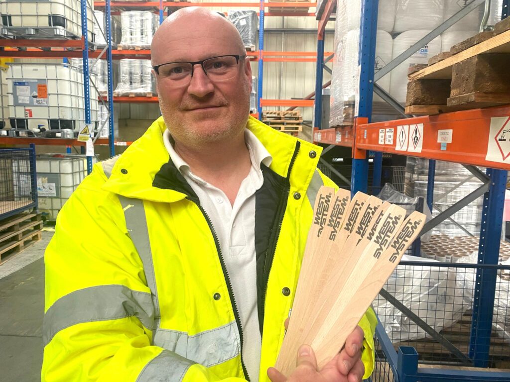 man in warehouse holding west system epoxy mixing sticks.