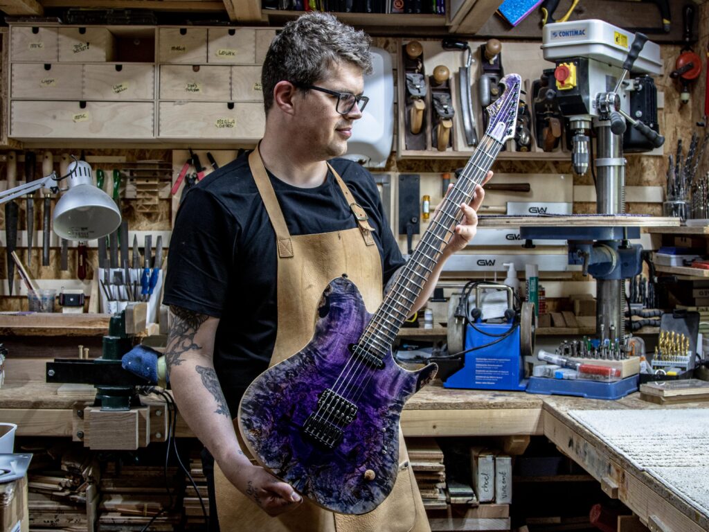 Maikel, holding a guitar he's made for his company Wel Guitars, stood in his workshop. 