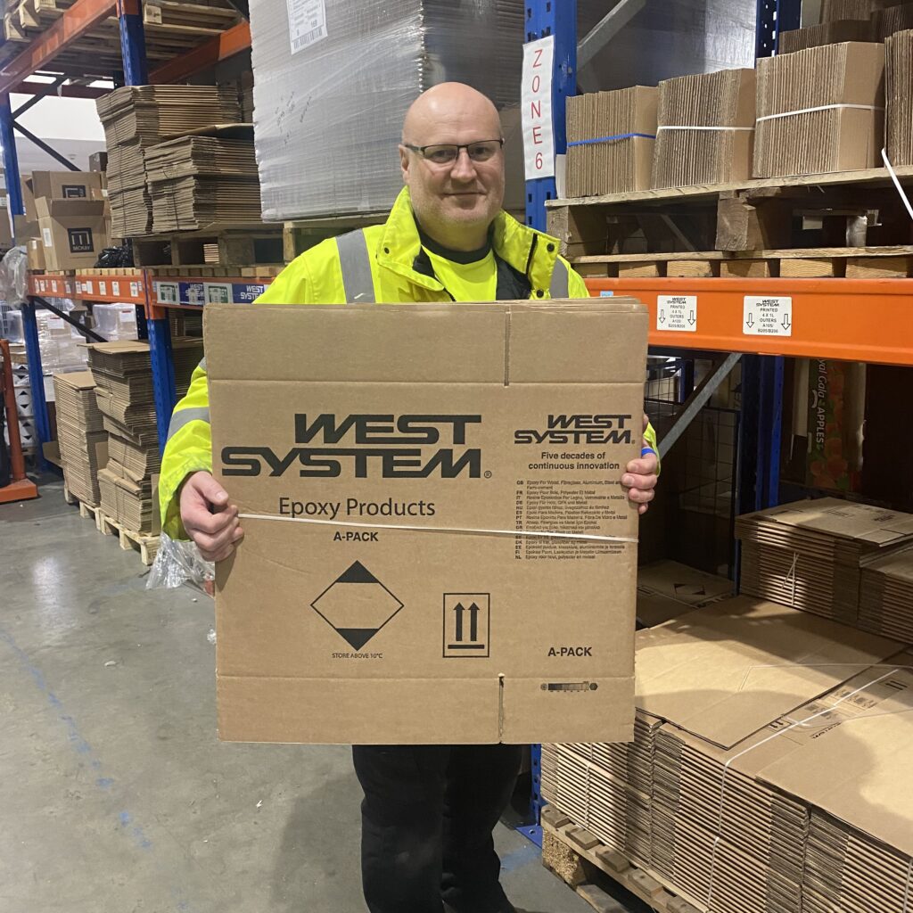 martin in warehouse holding up a west system cardboard box. 